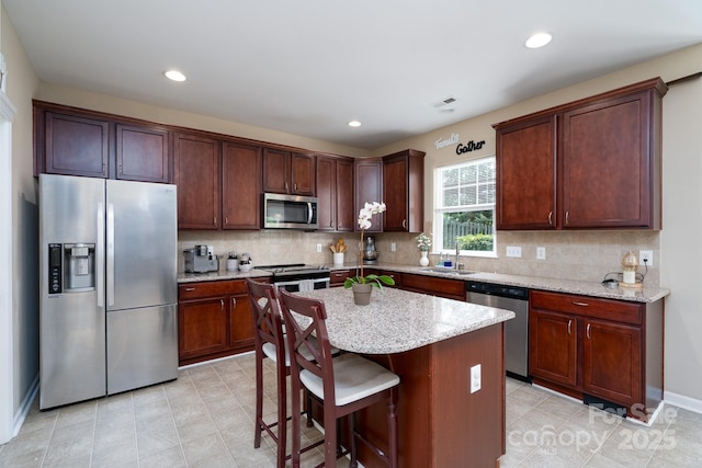 4915 Juniper Grove Ct SW, Concord, NC 28027 - kitchen with stainless steel appliances, light stone counters, decorative backsplash, a center island, and a breakfast bar area
