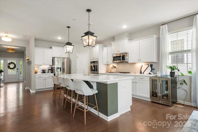 15515 Laverack Ln, Davidson, NC 28036 - kitchen featuring appliances with stainless steel finishes, beverage cooler, decorative backsplash, a kitchen island with sink, and dark wood-style flooring