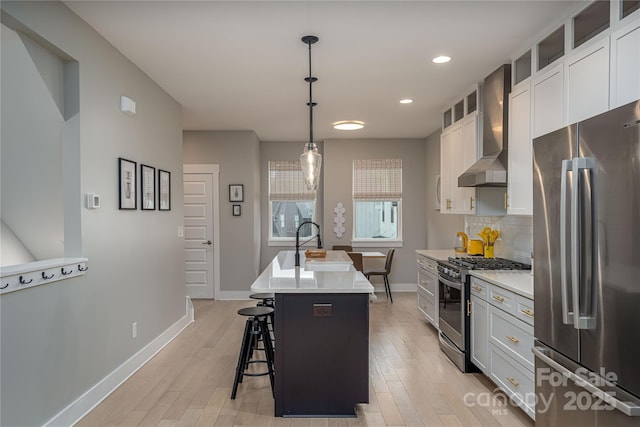 2011 Hamorton Pl, Charlotte, NC 28205 - kitchen featuring appliances with stainless steel finishes, wall chimney exhaust hood, baseboards, a kitchen island with sink, and light wood-style flooring