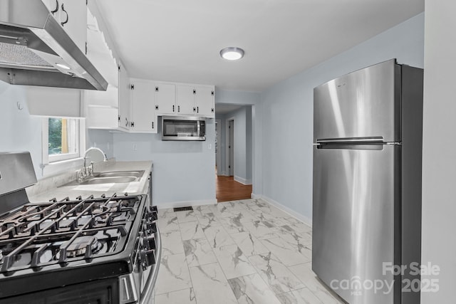 310 S Spencer Ave, Spencer, NC 28159 - kitchen featuring appliances with stainless steel finishes, range hood, light marble finish floors, white cabinets, and light countertops