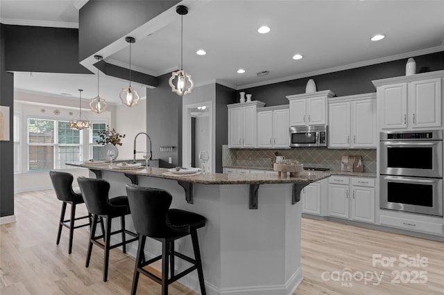 8725 Soaring Eagle Ln, Waxhaw, NC 28173 - kitchen with appliances with stainless steel finishes, light wood-type flooring, a kitchen bar, white cabinets, and backsplash