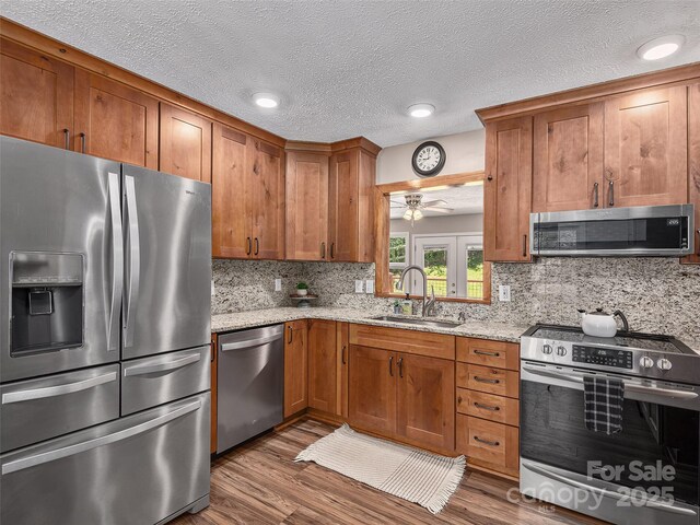 181 Junaluska Oaks Dr, Waynesville, NC 28786 - kitchen with stainless steel appliances, brown cabinetry, wood finished floors, light stone counters, and backsplash