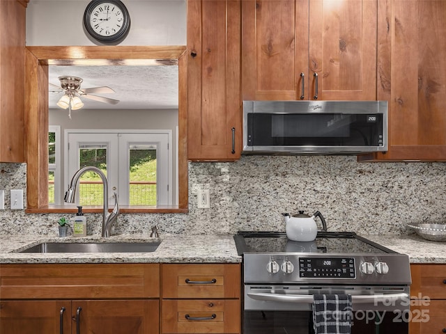 181 Junaluska Oaks Dr, Waynesville, NC 28786 - kitchen featuring appliances with stainless steel finishes, brown cabinetry, tasteful backsplash, light stone countertops, and a ceiling fan
