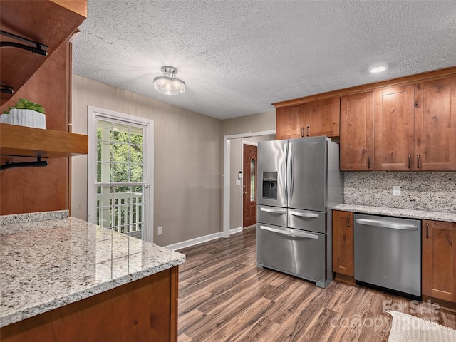 181 Junaluska Oaks Dr, Waynesville, NC 28786 - kitchen with stainless steel appliances, brown cabinetry, wood finished floors, a textured ceiling, and light stone countertops
