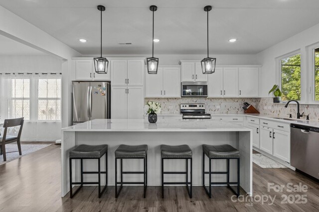 3127 Pinehills Way, Mount Holly, NC 28120 - kitchen featuring stainless steel appliances, a sink, white cabinets, a kitchen island, and tasteful backsplash