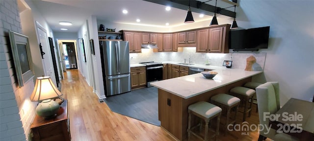 308 Woodfield Dr, Asheville, NC 28803 - kitchen with stainless steel appliances, a peninsula, under cabinet range hood, a breakfast bar, and light wood-style flooring