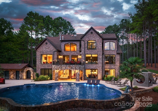 1220 Broadside Rd, York, SC 29745 - back of property at dusk with a balcony, a patio area, an outdoor pool, and brick siding