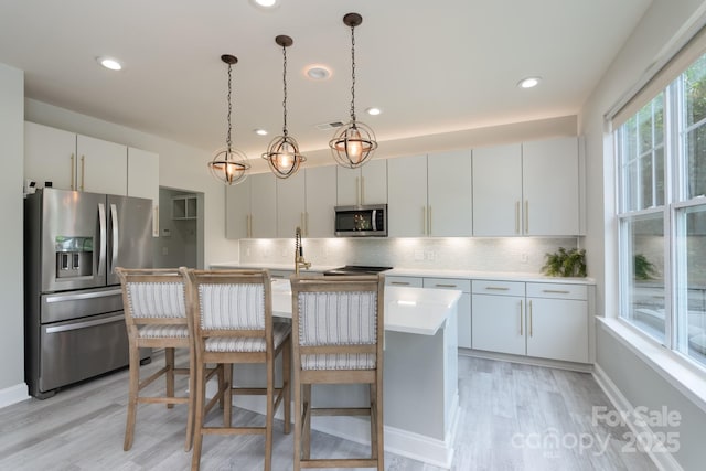 1211 Gold Rush Ct, Fort Mill, SC 29708 - kitchen featuring appliances with stainless steel finishes, light wood finished floors, tasteful backsplash, light countertops, and a kitchen island with sink