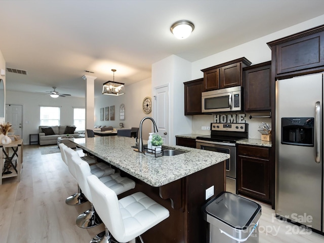 13422 Calloway Glen Dr, Charlotte, NC 28273 - kitchen featuring stainless steel appliances, a sink, dark brown cabinets, a breakfast bar area, and light stone countertops