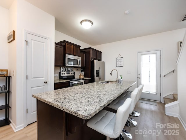 13422 Calloway Glen Dr, Charlotte, NC 28273 - kitchen featuring appliances with stainless steel finishes, a sink, a breakfast bar, dark brown cabinetry, and light wood-style flooring