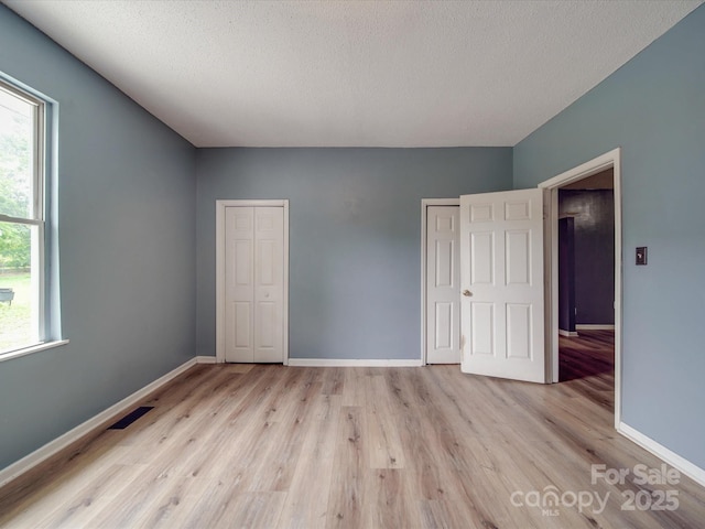 2440 Myers St, Gastonia, NC 28056 - unfurnished bedroom with two closets, light wood-style floors, baseboards, and a textured ceiling