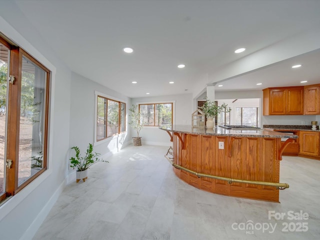 2143 Manawa Ln, Tega Cay, SC 29708 - kitchen featuring baseboards, a kitchen breakfast bar, light stone countertops, recessed lighting, and brown cabinetry