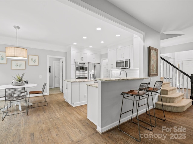 2821 Providence Spring Ln, Charlotte, NC 28270 - kitchen featuring appliances with stainless steel finishes, a peninsula, light stone countertops, white cabinets, and light wood finished floors