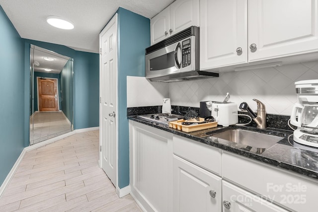 9550 Shore Dr Unit 930, Myrtle Beach, SC 29572 - kitchen with stainless steel microwave, baseboards, a sink, decorative backsplash, and white cabinetry