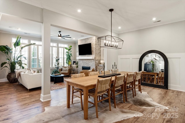 20216 Shaffer Bach Ln, Charlotte, NC 28277 - dining room featuring a fireplace, ceiling fan, a decorative wall, light wood finished floors, and a wainscoted wall