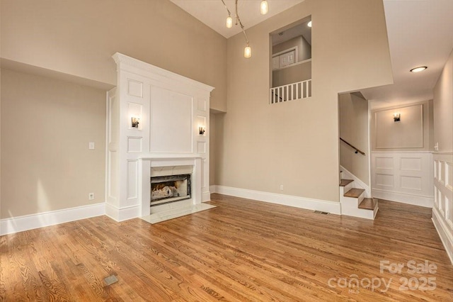 74 Eastmoor Dr, Asheville, NC 28805 - unfurnished living room with high vaulted ceiling, light wood-type flooring, stairway, a fireplace with flush hearth, and baseboards