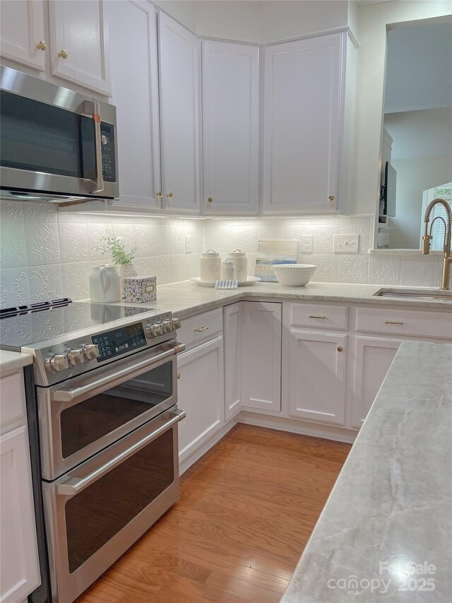 1006 Phar Lap Dr, Indian Trail, NC 28079 - kitchen with stainless steel appliances, a sink, white cabinets, tasteful backsplash, and light wood-style floors