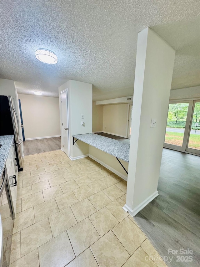 9541 Shannon Green Dr Unit C, Charlotte, NC 28213 - kitchen featuring a textured ceiling, freestanding refrigerator, baseboards, light stone countertops, and light tile patterned floors
