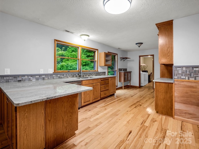 989 Mine Gap Rd, Zirconia, NC 28790 - kitchen featuring a peninsula, light wood-style flooring, tasteful backsplash, brown cabinetry, and a sink