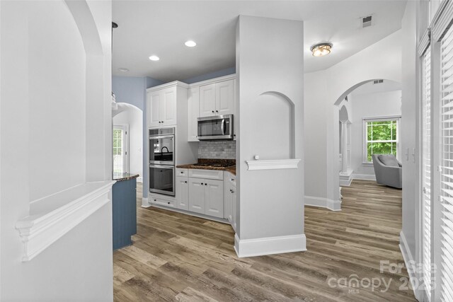 1009 Jerry Ln, Matthews, NC 28105 - kitchen with arched walkways, stainless steel appliances, white cabinetry, wood finished floors, and recessed lighting