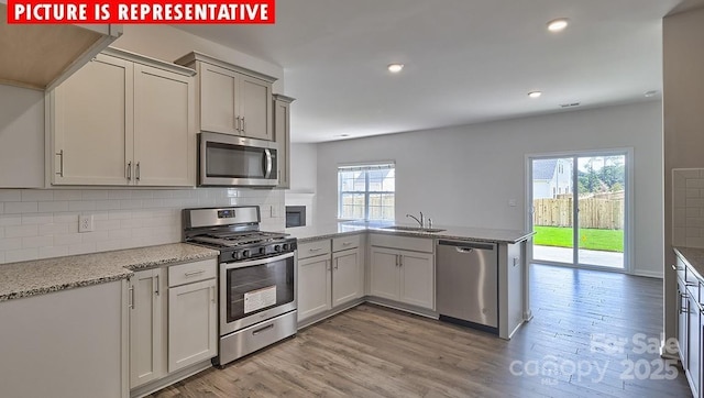 8036 Kennesaw Dr, Gastonia, NC 28056 - kitchen with appliances with stainless steel finishes, a peninsula, decorative backsplash, a sink, and light wood-type flooring