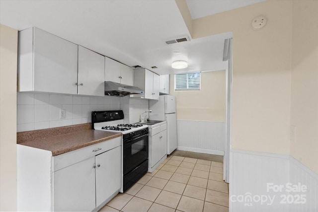 1810 13th Ave NE, Hickory, NC 28601 - kitchen featuring black gas range oven, under cabinet range hood, white cabinetry, freestanding refrigerator, and wainscoting