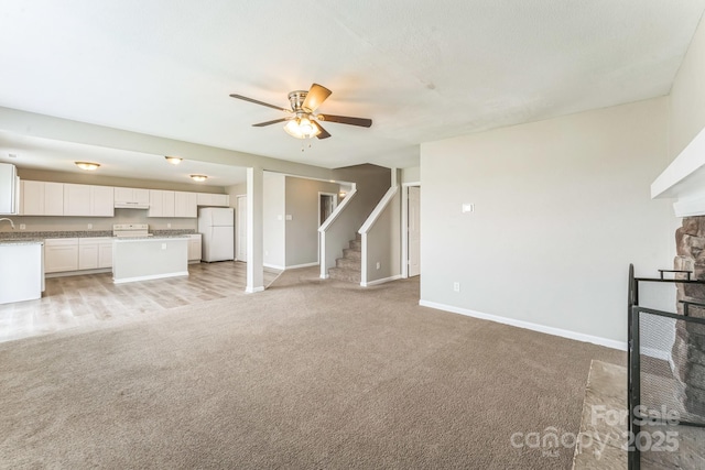 673 Shellbark Dr, Concord, NC 28025 - unfurnished living room with light colored carpet, a stone fireplace, baseboards, a ceiling fan, and stairs
