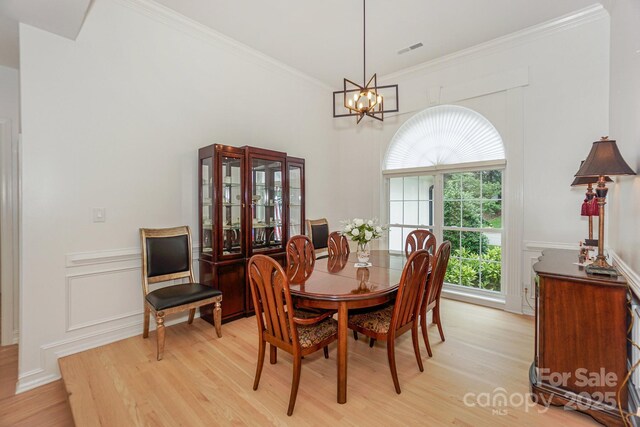 14831 Charterhouse Ln, Huntersville, NC 28078 - dining room featuring light wood-style floors, a chandelier, crown molding, a decorative wall, and wainscoting