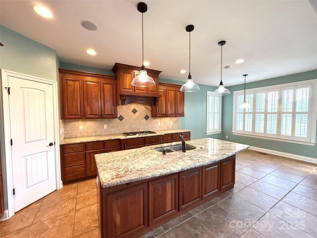 141 Weathers Creek Rd, Troutman, NC 28166 - kitchen with tasteful backsplash, gas cooktop, light stone counters, an island with sink, and brown cabinets