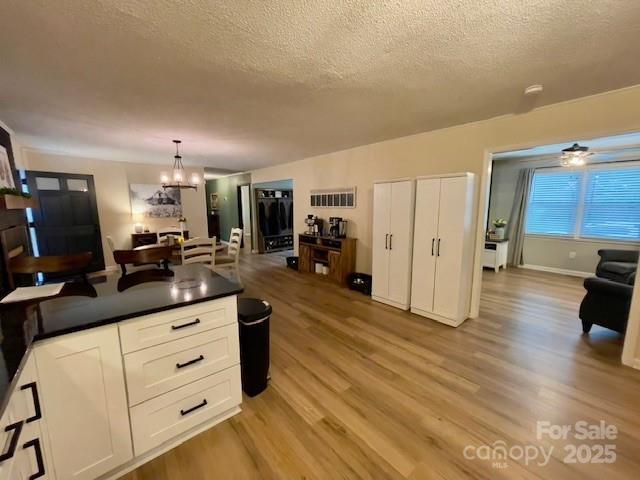135 Michelle Dr, Ellenboro, NC 28040 - kitchen with a textured ceiling, a chandelier, light wood-style floors, dark countertops, and white cabinets