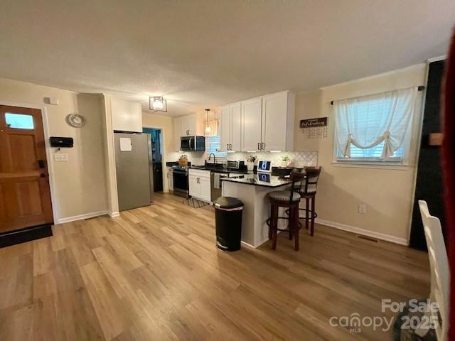 135 Michelle Dr, Ellenboro, NC 28040 - kitchen with stainless steel appliances, white cabinetry, a kitchen bar, a peninsula, and light wood-style floors