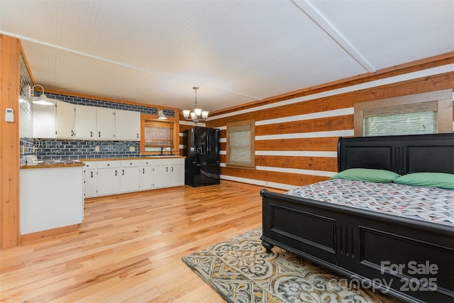 2709 Blythe Rd, Waxhaw, NC 28173 - bedroom featuring black fridge, a chandelier, wood walls, light wood-type flooring, and a sink