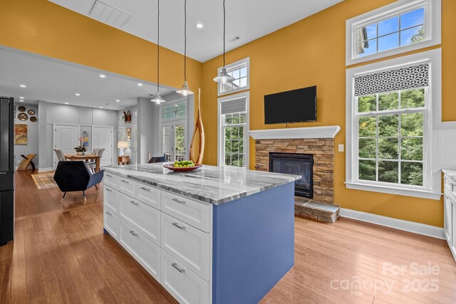 2009 Waterbury Ln, Waxhaw, NC 28173 - kitchen featuring open floor plan, white cabinetry, light wood-style flooring, light stone counters, and a fireplace