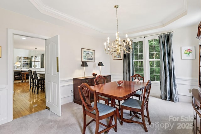 11103 Fountaingrove Dr, Charlotte, NC 28262 - carpeted dining area featuring a chandelier, a raised ceiling, ornamental molding, a decorative wall, and wainscoting