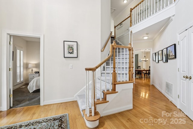 11103 Fountaingrove Dr, Charlotte, NC 28262 - staircase featuring wood finished floors, ornamental molding, a towering ceiling, a chandelier, and baseboards
