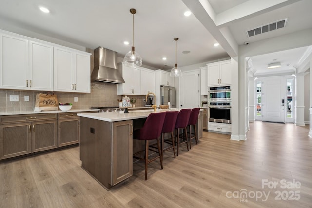 18129 Sulton Ter, Huntersville, NC 28078 - kitchen with wall chimney range hood, appliances with stainless steel finishes, a kitchen breakfast bar, decorative backsplash, and light wood-style floors