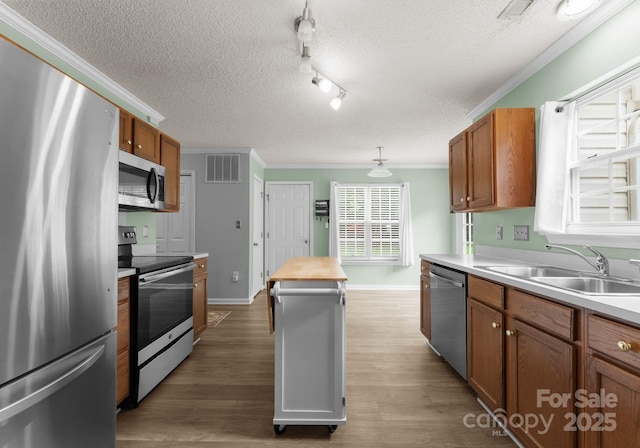 8808 Palmutum Pl, Charlotte, NC 28269 - kitchen with stainless steel appliances, a sink, crown molding, a textured ceiling, and brown cabinetry