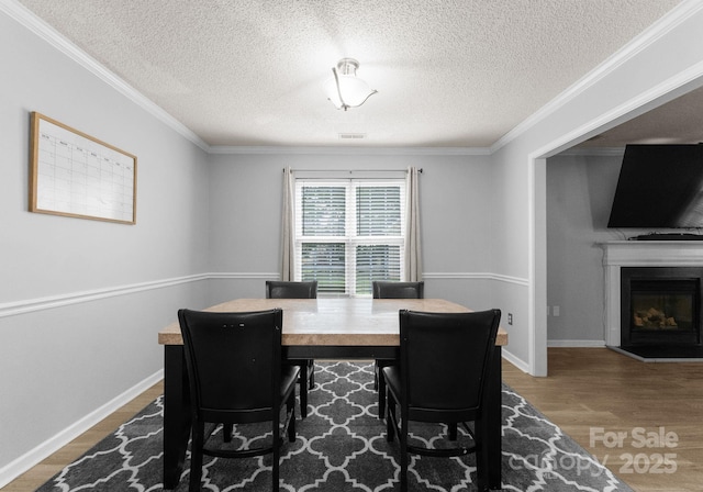 8808 Palmutum Pl, Charlotte, NC 28269 - dining space featuring wood finished floors, ornamental molding, a textured ceiling, a glass covered fireplace, and baseboards