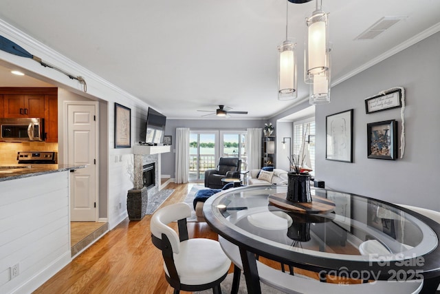 635 Portside Dr, Davidson, NC 28036 - dining space with light wood-type flooring, a glass covered fireplace, a ceiling fan, ornamental molding, and baseboards