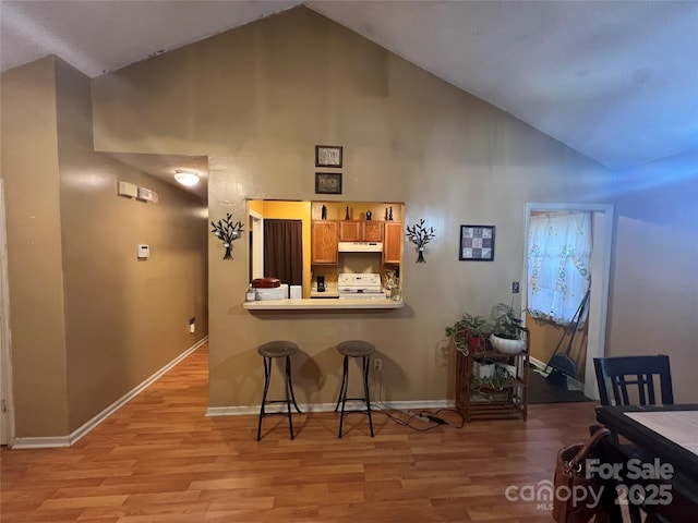 5816 Rocky Mount Ct, Charlotte, NC 28214 - kitchen with white range with electric stovetop, under cabinet range hood, light wood-style floors, high vaulted ceiling, and a breakfast bar