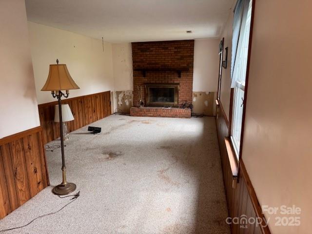 6561 Weldon Cir NW, Concord, NC 28027 - unfurnished living room featuring carpet, wainscoting, wooden walls, and a brick fireplace