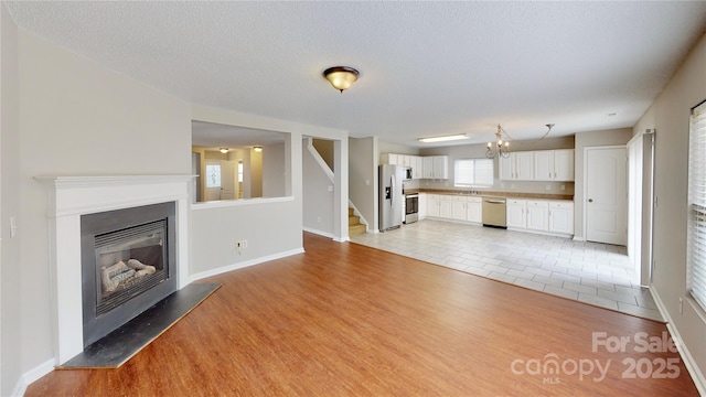 8139 Deodora Cedar Ln, Charlotte, NC 28215 - unfurnished living room featuring a glass covered fireplace, baseboards, light wood-style flooring, stairs, and a sink