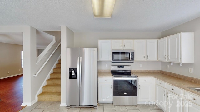 8139 Deodora Cedar Ln, Charlotte, NC 28215 - kitchen featuring stainless steel appliances, white cabinetry, light countertops, light tile patterned flooring, and a textured ceiling