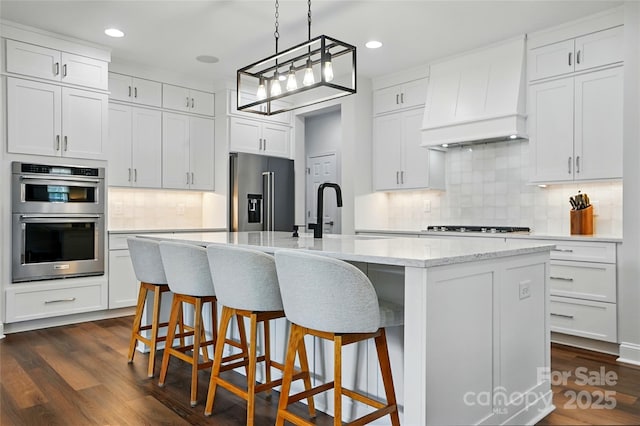 7322 Vesper Dr, Huntersville, NC 28078 - kitchen featuring appliances with stainless steel finishes, premium range hood, tasteful backsplash, a kitchen island with sink, and white cabinets