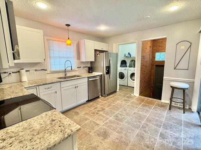7133 Tall Tree Ln, Charlotte, NC 28214 - kitchen featuring separate washer and dryer, a sink, appliances with stainless steel finishes, a textured ceiling, and white cabinetry