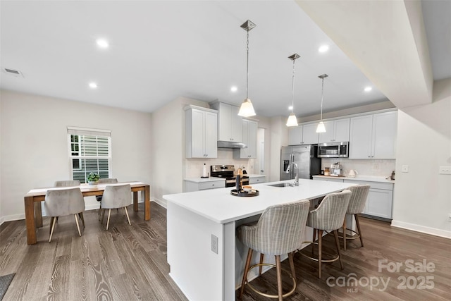 1022 Hinson Forest Rd, Monroe, NC 28110 - kitchen featuring appliances with stainless steel finishes, dark wood-type flooring, a kitchen island with sink, under cabinet range hood, and light countertops