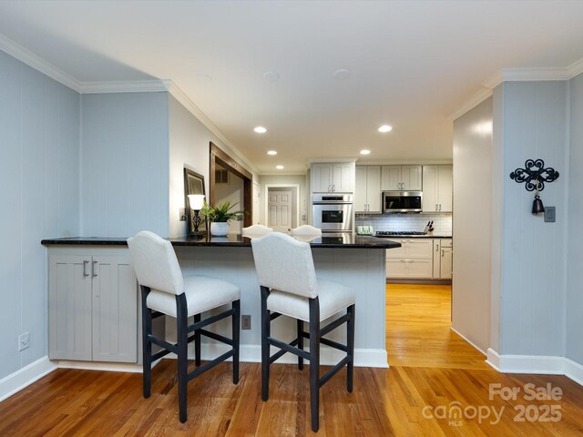 6941 Queensberry Dr, Charlotte, NC 28226 - kitchen featuring stainless steel appliances, a breakfast bar area, light wood-style flooring, backsplash, and dark countertops