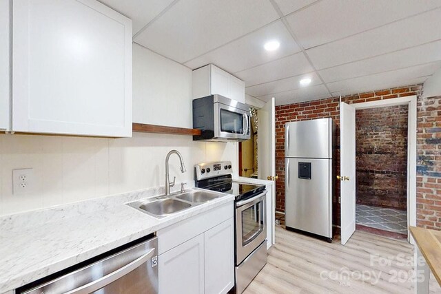 495 Fairview Rd, Asheville, NC 28803 - kitchen featuring stainless steel appliances, brick wall, a sink, light wood-style floors, and white cabinetry