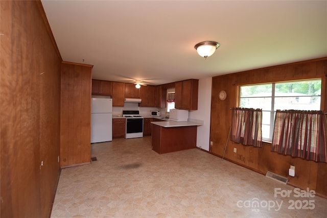 908 Ravendale Dr, Charlotte, NC 28216 - kitchen featuring white appliances, wooden walls, under cabinet range hood, brown cabinets, and a peninsula