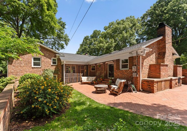 1226 Tarrington Ave, Charlotte, NC 28205 - back of house featuring brick siding, an outdoor living space, a patio, a chimney, and a sunroom